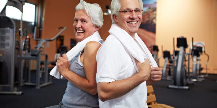 Lachendes Seniorenpaar im Fitnesscenter lehnt sich aneinander an