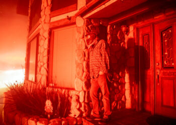 A man watches his neighbor's home burn from his front porch during the Hillside fire in the North Park neighborhood of San Bernardino, California on October 31, 2019. (Photo by Josh Edelson / AFP)