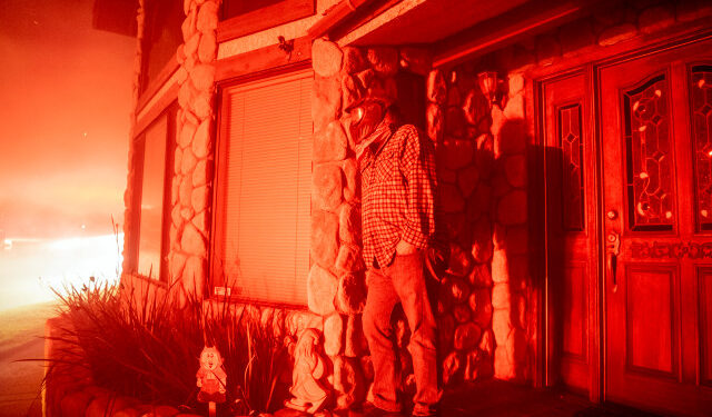 A man watches his neighbor's home burn from his front porch during the Hillside fire in the North Park neighborhood of San Bernardino, California on October 31, 2019. (Photo by Josh Edelson / AFP)