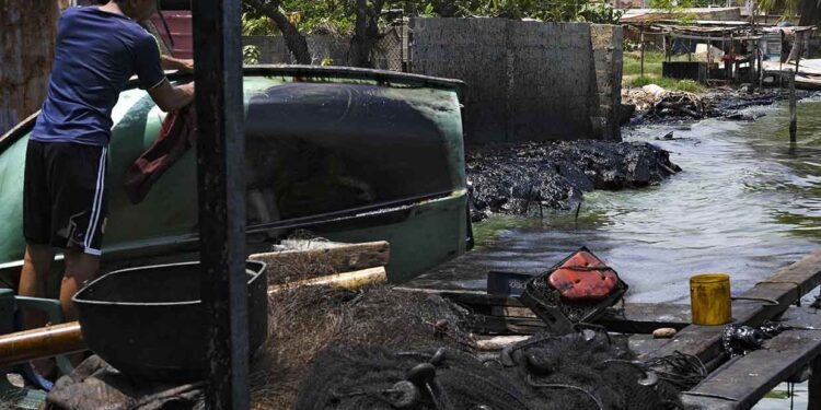 A fisherman cleans the oil smeared on his boat on the banks of the polluted Maracaibo Lake, in Cabimas, near Maracaibo, Zulia state, Venezuela, on June 13, 2019. - The city of Maracaibo is the center of the country's oil industry, and its lake is an eternal oil spill. (Photo by YURI CORTEZ / AFP)