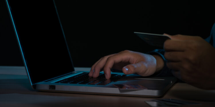 Cyber crime concept: Anonymous man holding credit card with laptop on his hand