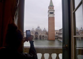 A woman takes a photo of the flooded St. Mark's Square, with St. Mark's Basilica (Rear) and the Bell Tower on November 15, 2019 in Venice, two days after the city suffered its highest tide in 50 years. - Flood-hit Venice was bracing for another exceptional high tide on November 15, as Italy declared a state of emergency for the UNESCO city where perilous deluges have caused millions of euros worth of damage. (Photo by Filippo MONTEFORTE / AFP)