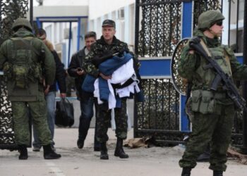 Ukrainian officers leave as Russian soldiers stand guard at the Ukrainian navy headquarters in the Crimean city of Sevastopol on March 19, 2014.  Ukrainian servicemen filed out of navy headquarters in Sevastopol on Wednesday with tears in their eyes after the base was seized by pro-Moscow militants, Russian troops and Cossack forces.  The assault began when some 200 unarmed militants -- some of them in balaclavas -- sawed through a fence and overran the base while the Ukrainian servicemen barricaded themselves inside.  AFP PHOTO/  VIKTOR DRACHEV