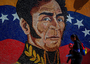 AME7169. CARACAS (VENEZUELA), 25/02/2020.- Fotografía del 11 de febrero del 2020 donde se observa un mural con la imagen del héroe nacional Simón Bolivar mientras una mujer camina con un niño que usa una mascara del hombre araña en Caracas (Venezuela). Simón Bolívar ha renacido cada vez que un líder venezolano necesitaba desempolvar viejas glorias o dar lustre a un gobierno. Su última resurrección fue a lomos de una revolución de aspiración socialista que lo forjó a su imagen y semejanza para devolverlo a las escuelas transformado en su icono. EFE/MIGUEL GUTIERREZ