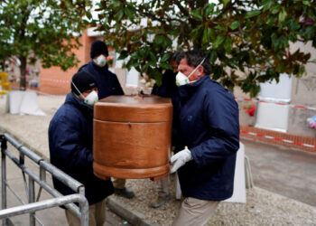 Employees of a mortuary carry the coffin of a person who died from the coronavirus disease (COVID-19), during the partial lockdown to combat the disease outbreak, at the Carabanchel cemetery in Madrid, Spain, March 27, 2020. REUTERS/Juan Medina