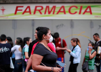 A woman wears a protective mask while people queue outside the pharmacy in response to coronavirus (COVID-19) spread, in Caracas, Venezuela March 13, 2020. REUTERS/Carlos Jasso