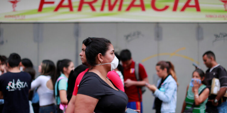 A woman wears a protective mask while people queue outside the pharmacy in response to coronavirus (COVID-19) spread, in Caracas, Venezuela March 13, 2020. REUTERS/Carlos Jasso