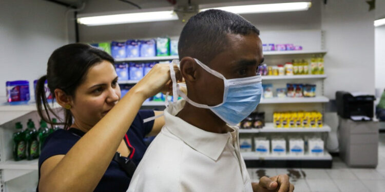 A woman helps a man to put a face mask on, as Venezuelans rush to buy hand sanitizers and masks in the face of the global COVID-19 coronavirus pandemic, in Caracas, on March 13, 2020. (Photo by CRISTIAN HERNANDEZ / AFP)