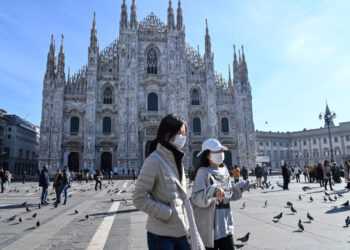 Two women wearing a protective facemask walk across the Piazza del Duomo, in front of the Duomo, in central Milan, on February 24, 2020 closed following security measures taken in northern Italy against the COVID-19 the novel coronavirus. - Italy reported on February 24, 2020 its fourth death from the new coronavirus, an 84-year old man in the northern Lombardy region, as the number of people contracting the virus continued to mount. (Photo by ANDREAS SOLARO / AFP)
