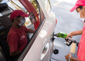 A worker of a gas station fills the tank of a car with gasoline wearing a face mask as a precautionary measure against the spread of the new coronavirus, COVID-19, in Caracas on March 23, 2020. - Venezuela is facing the novel coronavirus pandemic while suffering a major gasoline shortage and with the country's water system collapsed, which has left many homes without running water. (Photo by Cristian Hernandez / AFP)