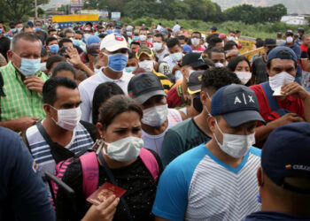 People wearing protective face masks line up to cross the border between Colombia and Venezuela at the Simon Bolivar international bridge, after the World Health Organization has described the outbreak as a pandemic, in Cucuta, Colombia March 12, 2020.  REUTERS/Carlos Eduardo Ramirez