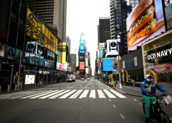 A man bikes through the deserted Times Square on April 10, 2020 in New York City. - The global coronavirus death toll topped 100,000 on April 10 as Easter celebrations around the world kicked off in near-empty churches with billions of people stuck indoors to halt the pandemic's deadly worldwide march. (Photo by Johannes EISELE / AFP)