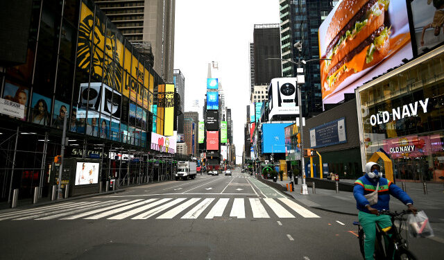 A man bikes through the deserted Times Square on April 10, 2020 in New York City. - The global coronavirus death toll topped 100,000 on April 10 as Easter celebrations around the world kicked off in near-empty churches with billions of people stuck indoors to halt the pandemic's deadly worldwide march. (Photo by Johannes EISELE / AFP)