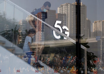 A man and a child wearing face masks following the coronavirus disease (COVID-19) outbreak walk past a 5G sign inside a Huawei store at a shopping mall in Beijing, China July 14, 2020.  REUTERS/Tingshu Wang