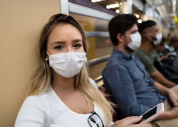 Young woman uses cellphone inside the train car. Traveler wears mask to prevent spread of CoroVirus, Covid-19