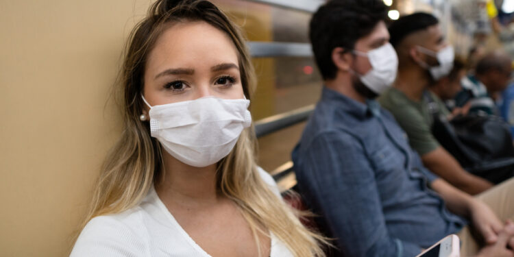 Young woman uses cellphone inside the train car. Traveler wears mask to prevent spread of CoroVirus, Covid-19