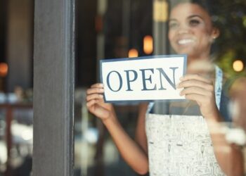 Cropped shot of a young woman hanging up an open sign on the window of her cafe