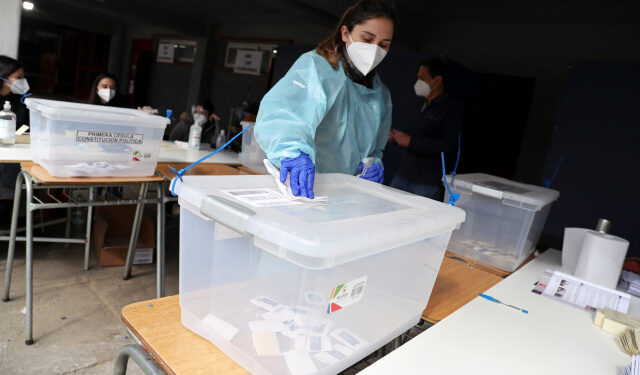 A woman wearing a protective face mask and a suit disinfects a ballot box during a referendum on a new Chilean constitution in Santiago, Chile, October 25, 2020. REUTERS/Ivan Alvarado