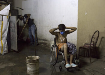 Johan Medina (R), 31, puts on a face mask after taking a bath, as one of his neighbors (L) sweeps dirty water to a drain at a shelter located in the basement of the Sudameris public building in Caracas, on October 9, 2020, amid the new coronavirus pandemic. - Fourteen families live without electricity, ventilation, running water or bathrooms in the basement of a government building in Caracas, which makes them specially vulnerable to the coronavirus. (Photo by Cristian Hernandez / AFP)