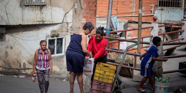 Alexandra Armijo (c), de 22 años, cambia plátanos por arroz en un barrio de Catia, el 20 de enero de 2021 en Caracas (Venezuela). Como si de un deporte extremo se tratase, Bryan, Samuel y Alexandra caminan las empinadas calles del barrio caraqueño de Catia con una cesta a cuestas cargada con plátanos. El objetivo: intercambiarlos por productos que luego venderán para poder sobrevivir en medio de la severa crisis económica venezolana. El trueque del siglo XXI. EFE/RAYNER PEÑA R