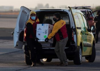 Dos trabajadores de un servicio de mensajería cargaban una caja con las primeras 10.000 dosis de la vacuna contra la covid-19 en llegar a territorio chileno, el pasado 24 de diciembre. EFE/Alberto Valdés/Archivo