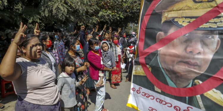 Demonstrators shout slogan and flash three-fingered salute, a symbol of resistance against the military coup standing next to a defaced image of Myanmar military Commander-in-Chief Senior Gen. Min Aung Hlaing in Mandalay, Myanmar on Wednesday, Feb. 10, 2021. Protesters continued to gather Wednesday morning in Mandalay breaching Myanmar's new military rulers' decrees that effectively banned peaceful public protests in the country's two biggest cities. (AP Photo)