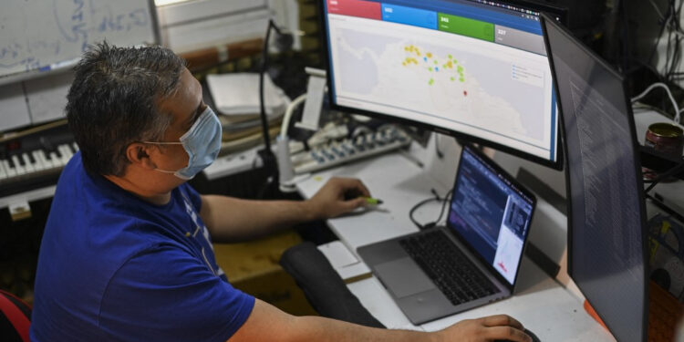 Venezuelan Jose Miguel Avendano, works on his computers as he shows an application designed by him that allows locating health centers and hospitals as well as the most feasible route to reach them in the case of emergencies due to the COVID-19 in the La Candelaria neighborhood, Caracas on May 11, 2021. - A database of clinics and hospitals, a biosecurity catalogue for businesses or a medicine and oxygen directory. Apps created by Venezuelans against COVID-19 emerge amidst the economic crisis and a virulent second wave of contagions. (Photo by Yuri CORTEZ / AFP)