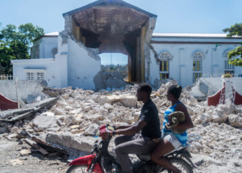 People drive past the remains of the "Sacré coeur des Cayes" church in Les Cayes on August 15, 2021, after a 7.2-magnitude earthquake struck the southwest peninsula of the country. - Hunched on benches, curled up in chairs or even lying the floor, those injured in the powerful earthquake that wreaked havoc on Haiti on Saturday crowded an overburdened hospital near the epicenter. The emergency room in Les Cayes, in southwestern Haiti, which was devastated by the 7.2-magnitude quake on Saturday morning that killed at least 724 people, is expecting reinforcements to help treat some of the thousands of injured. (Photo by Reginald LOUISSAINT JR / AFP)