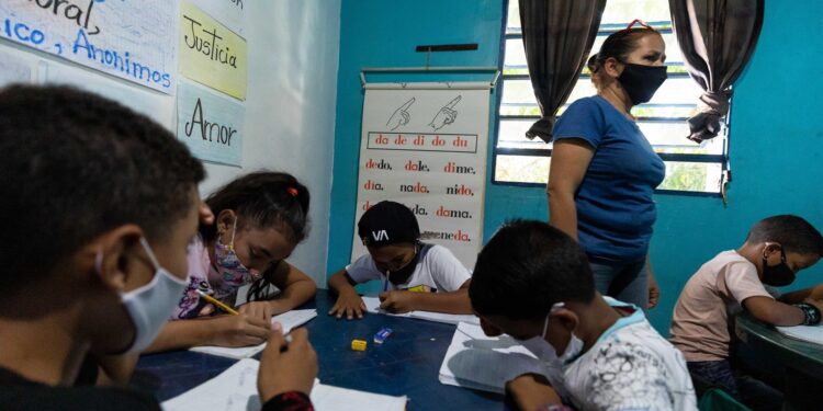 Niños hacen tareas en sus cuadernos durante una clase en la casa de la maestra Jasmín Castro, el 20 de agosto de 2021, en Petare, Caracas (Venezuela). Maestras preocupadas por la educación de los niños que habitan en Petare, una de las barriadas más pobres de Venezuela, abrieron las puertas de sus casas para educar a los chicos en medio del cierre de escuelas, empujado por la covid-19, que ya suma más de un año y el difícil acceso a internet. EFE/ RAYNER PEÑA R.