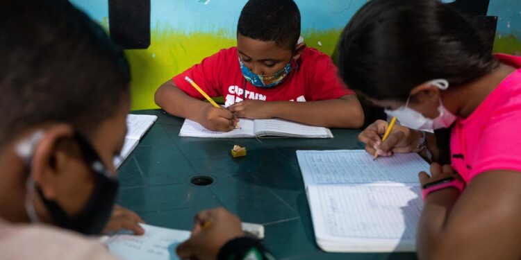 Niños hacen tareas en sus cuadernos durante una clase en la casa de la maestra Jasmín Castro, el 20 de agosto de 2021, en Petare, Caracas (Venezuela). Maestras preocupadas por la educación de los niños que habitan en Petare, una de las barriadas más pobres de Venezuela, abrieron las puertas de sus casas para educar a los chicos en medio del cierre de escuelas, empujado por la covid-19, que ya suma más de un año y el difícil acceso a internet. EFE/ RAYNER PEÑA R.