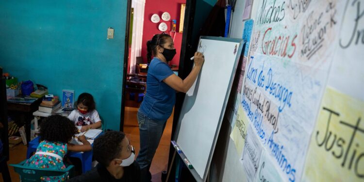 CARACAS (VENEZUELA), 23/08/2021.- La maestra Jasmín Castro escribe en una pizarra durante una clase en su casa, el 20 de agosto de 2021, en Petare, Caracas (Venezuela). Maestras preocupadas por la educación de los niños que habitan en Petare, una de las barriadas más pobres de Venezuela, abrieron las puertas de sus casas para educar a los chicos en medio del cierre de escuelas, empujado por la covid-19, que ya suma más de un año y el difícil acceso a internet. EFE/ RAYNER PEÑA