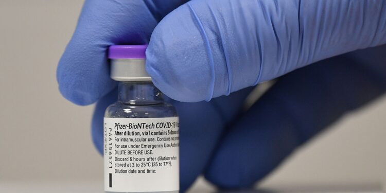 Mano con guantes sostiene una vacuna contra la COVID-19 de Pfizer-BioNTech