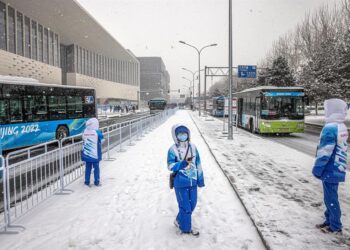 Voluntarios olímpicos se paran en una estación de autobuses frente al centro de medios olímpico, que forma parte de la 'burbuja' olímpica COVID-19, en un día nevado, durante los Juegos Olímpicos de Pekín 2022 en Pekín, China. EFE/EPA/PILIPEY ROMANA