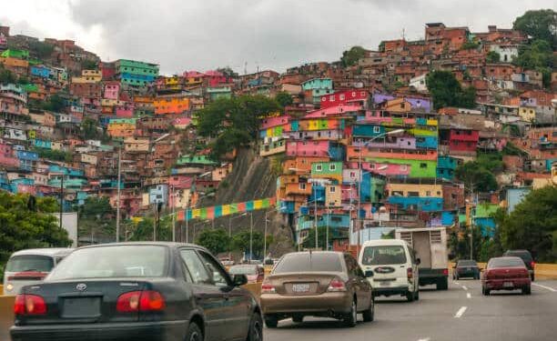 Photograph taken in Caracas, Venezuela, on September 2, 2015 where you can see a high traffic road with many vehicles being hours of noon. You see the white streaks on the asphalt, the road public lighting and on the sides a great overcrowding of very colorful popular housing or more commonly called "ranchos" whose characteristics of poverty do not allow them to have all the comforts and security of a standard home.