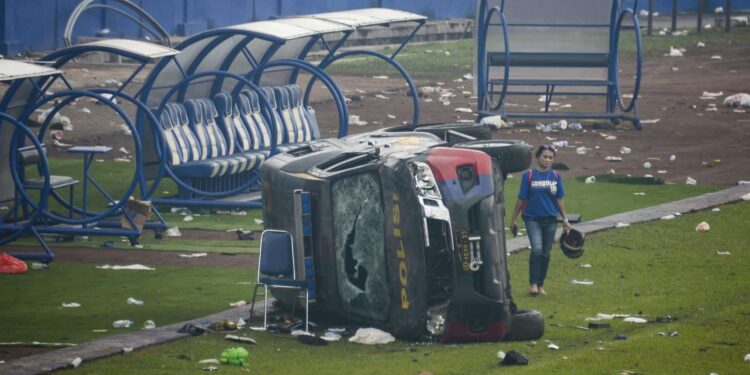 Una mujer pasa junto a un vehículo de la policía destrozado tras los disturbios en un partido de fútbol en el estadio Kanjuruhan de Malang, que han dejado al menos 174 muertos. El brote de violencia se produjo después de que cerca de 3.000 aficionados del equipo Arema irrumpieran en el campo tras la derrota 2-3 sufrida ante el rival Persebaya Surabaya y chocaran con las fuerzas de seguridad, que a su vez utilizaron gases lacrimógenos en un intento de dispersar la multitud. EFE/ Sandi Sadewa