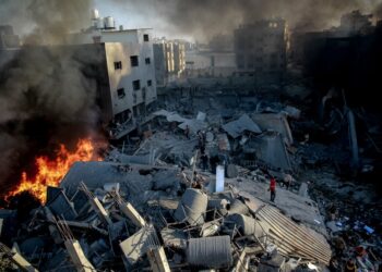 Smoke and fire rise from a levelled building as people gather amid the destruction in the aftermath of an Israeli strike on Gaza City on October 26, 2023, as battles continue between Israel and the Palestinian Hamas group. (Photo by Omar El-Qattaa / AFP)