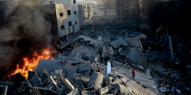 Smoke and fire rise from a levelled building as people gather amid the destruction in the aftermath of an Israeli strike on Gaza City on October 26, 2023, as battles continue between Israel and the Palestinian Hamas group. (Photo by Omar El-Qattaa / AFP)