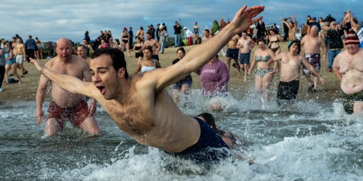 Revelers take part in the annual L-Street Brownies cold water plunge at M Street beach on New Years Day, January 1, 2024 in Boston, Massachusetts. The plunge on New Year's day dates back over 100 years in Boston. Monies from T-shirt sales are to be given to local charities.  The National Oceanic and Atmospheric Administration (NOAA) reported the water temp in Boston Harbor to be at 44.6F (7C) and air was measured at 30F (-1C). (Photo by Joseph Prezioso / AFP)