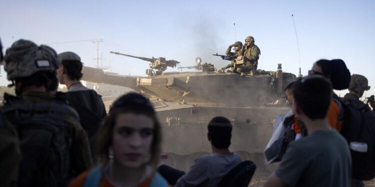 An Israeli battle tank rolls past right wing activists near the Erez crossing as they rally calling for the building of Israeli settlements in Gaza, on February 29, 2024, amid ongoing battles between Israel and the Palestinian militant group Hamas. (Photo by Oren ZIV / AFP)
