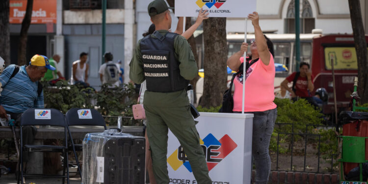 AME9819. CARACAS (VENEZUELA), 18/03/2024.- Trabajadores de Consejo Nacional Electoral (CNE) y miembros de la milicia arman un puesto de registro electoral este lunes, en Caracas (Venezuela). El Consejo Nacional Electoral (CNE) de Venezuela comenzó este lunes la jornada de inscripción y actualización de datos de votantes, en unos 300 puntos en todo el país, de cara a las elecciones presidenciales del próximo 28 de julio. Los jóvenes con 18 años cumplidos, y todos los que deseen actualizar sus datos por cambio de residencia, podrán acudir a una de estas sedes desde este lunes hasta el próximo 16 de abril, dentro y fuera del país. EFE/ Rayner Peña R.