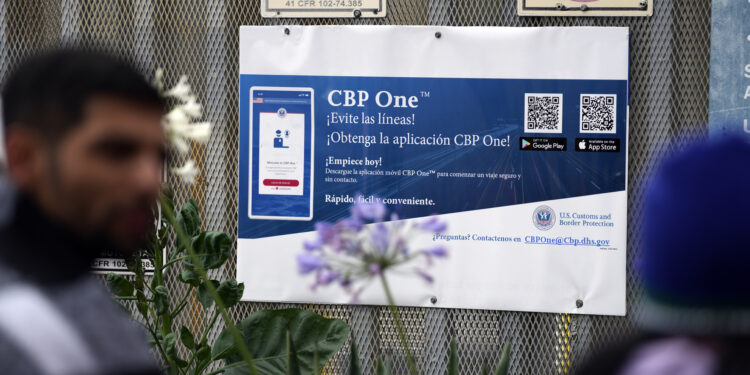 People waiting to apply for asylum stand in front or a sign for the CBP One app as they camp near the pedestrian entrance to the San Isidro Port of Entry, linking Tijuana, Mexico with San Diego, Thursday, June 1, 2023, in Tijuana, Mexico. U.S. authorities raised the number of people allowed to enter the country with an online app allows asylum-seekers to enter the country with appointments to 1,250 a day from 1,000 though demand still far outstrips supply. (AP Photo/Gregory Bull)