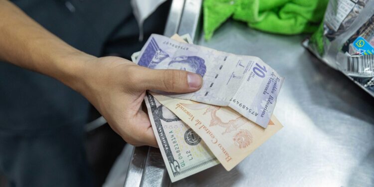 AME463. CARACAS (VENEZUELA), 09/07/2024.- Un hombre paga en una tienda con billetes de dolares estadounidenses y bolívares soberanos, el 8 de julio de 2024, en Caracas (Venezuela). La inflación en Venezuela, que en junio cayó hasta el 1 %, se ha desacelerado a raíz de una política para estabilizar el precio del dólar -divisa usada en el país para cotizar bienes y servicios-, para lo que también se han "sacrificado" salarios y créditos bancarios, advierten expertos. EFE/ Ronald Peña