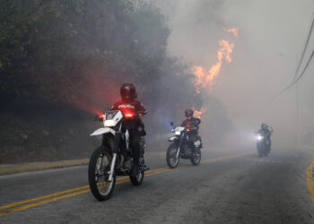 AME2229. QUITO (ECUADOR), 24/09/2024.- Policías patrullan en moto cerca a un incendio forestal este martes, Guapulo, Quito (Ecuador). Varios incendios forestales en los alrededores de Quito, la capital de Ecuador, han teñido con una espesa capa de humo a la ciudad, por lo que la autoridades han lanzado una alerta por la mala calidad del aire, sobre todo en el norte de la ciudad. EFE/ Santiago Fernández