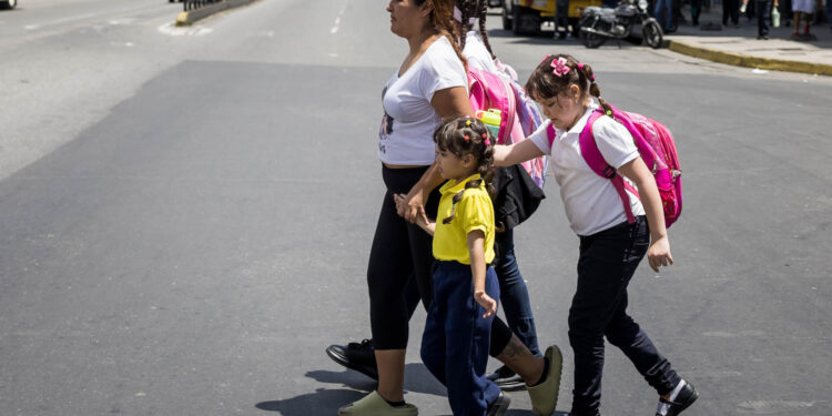 AME8516. CARACAS (VENEZUELA), 18/10/2024.- Fotografía del 10 de octubre del 2024 de una mujer caminando con unas niñas vestidas con uniforme escolar, en Caracas (Venezuela). La educación pública en Venezuela está en "emergencia" debido, entre otras razones, a la escasez de docentes, según el gremio, una situación que el Gobierno intenta resolver con varios programas, entre los que destaca un llamado a jubilados a reincorporarse y varias ofertas que buscan convencer a los maestros que dejaron las aulas por los bajos salarios. EFE/ Miguel Gutierrez