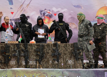 Israeli hostages Avera Mengistu (4th-R) and Tal Shoham (L) are flanked by Palestinian Hamas fighters as they stand on a stage during their release in Rafah in the southern Gaza Strip on February 22, 2025. Masked militants paraded Tal Shoham and Avera Mengistu on stage in the southern Gazan city of Rafah before handing them over to officials from the Red Cross. (Photo by Omar AL-QATTAA / AFP)